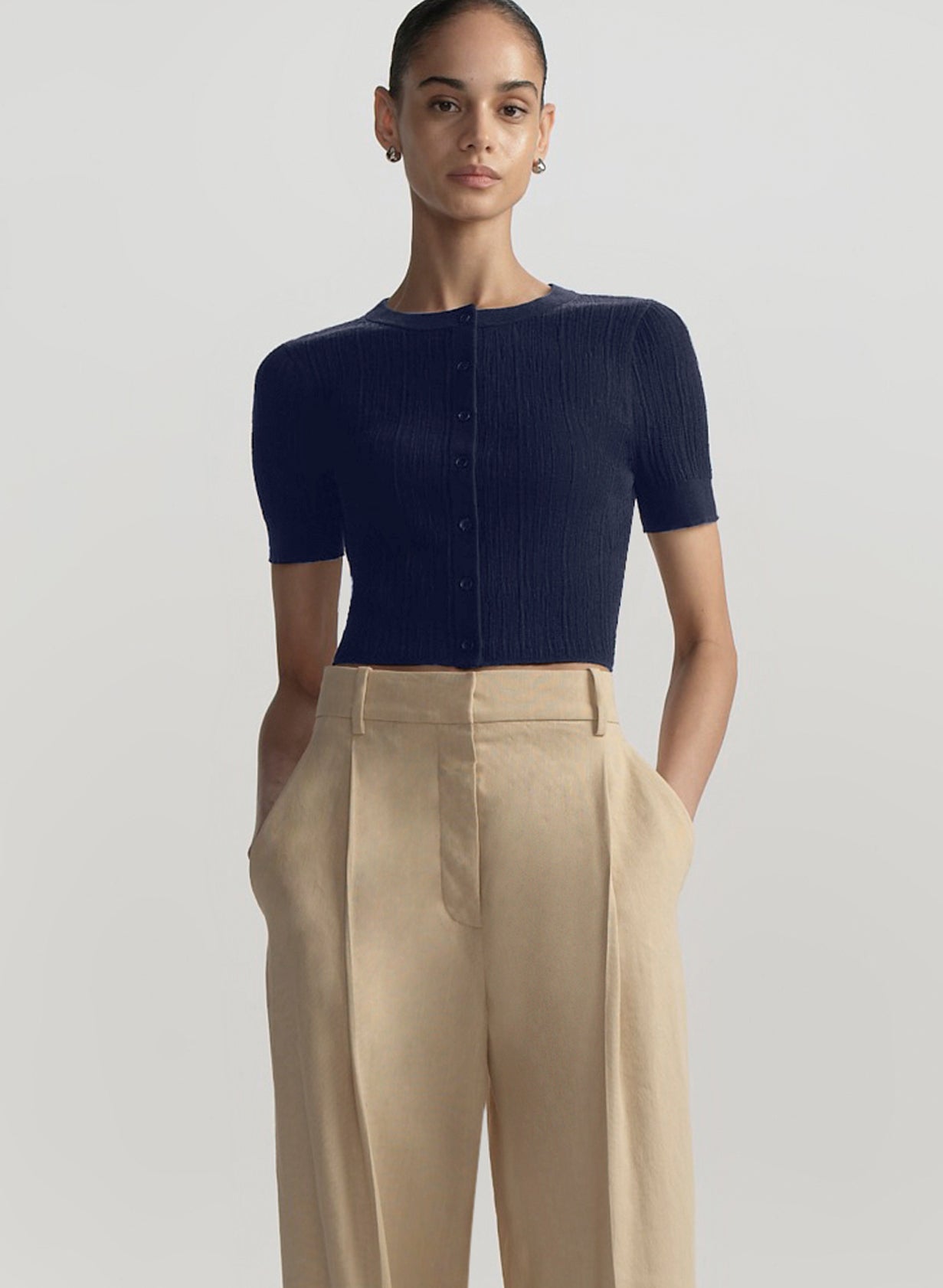 woman wearing cropped short sleeve cardigan in navy blue with tan pants