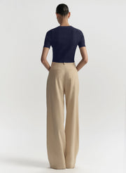 A model shown from the back wearing a navy blue short-sleeve ribbed knit top and beige wide-leg trousers, photographed against a clean white studio background.