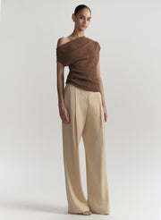 Model wearing a brown off-shoulder top and beige pants on a light gray background