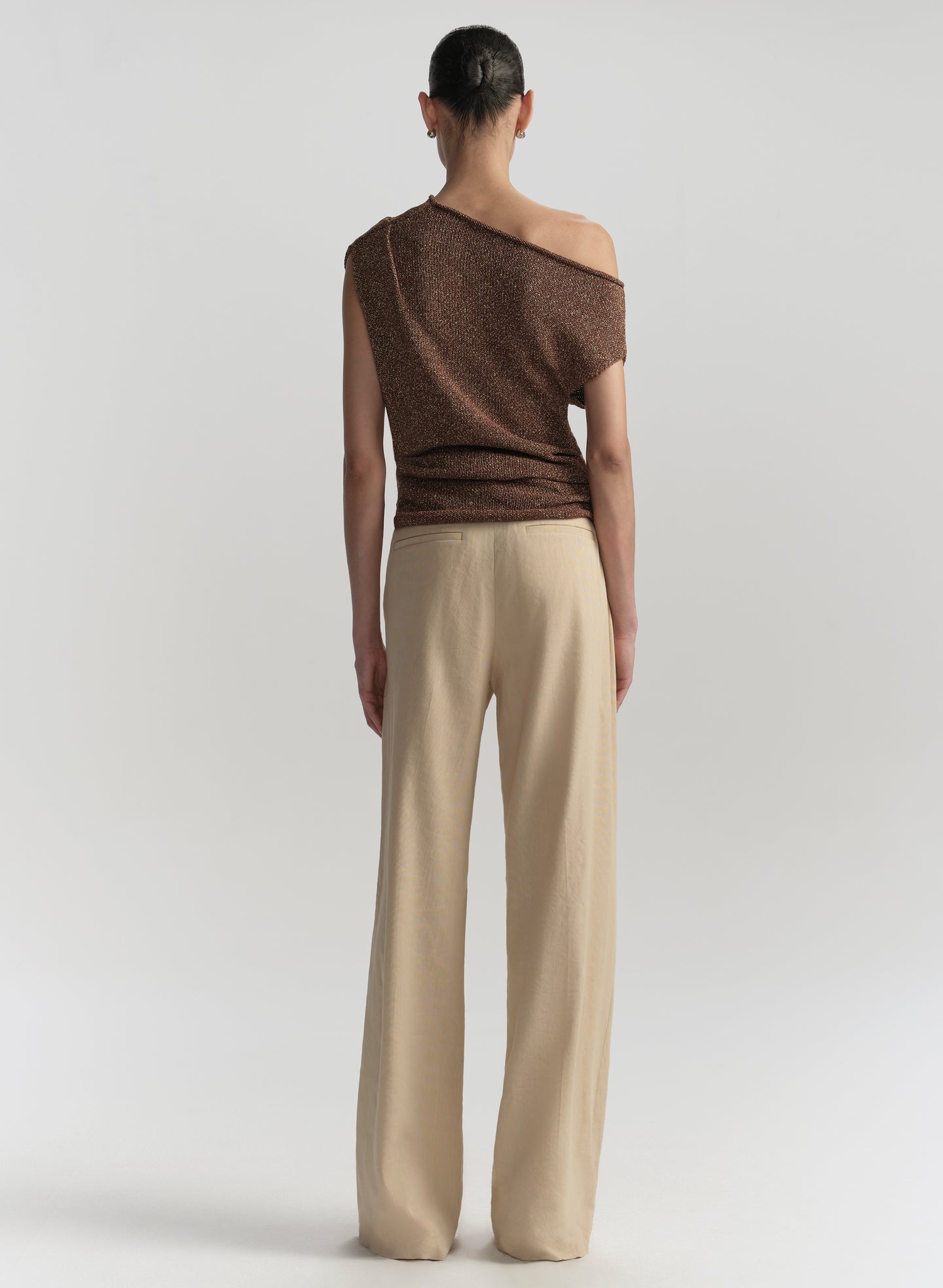 Woman wearing a brown off-shoulder top and beige pants on a white background