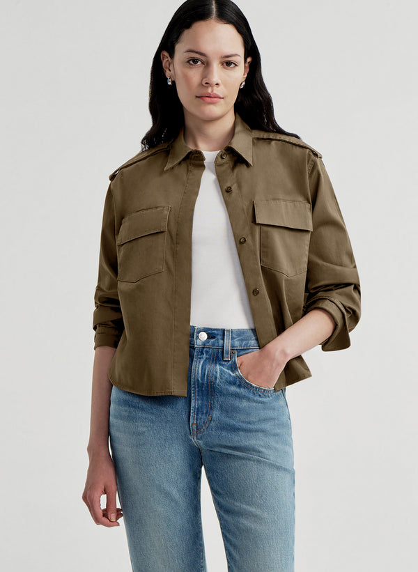 Woman wearing a brown jacket and blue jeans on a light gray background