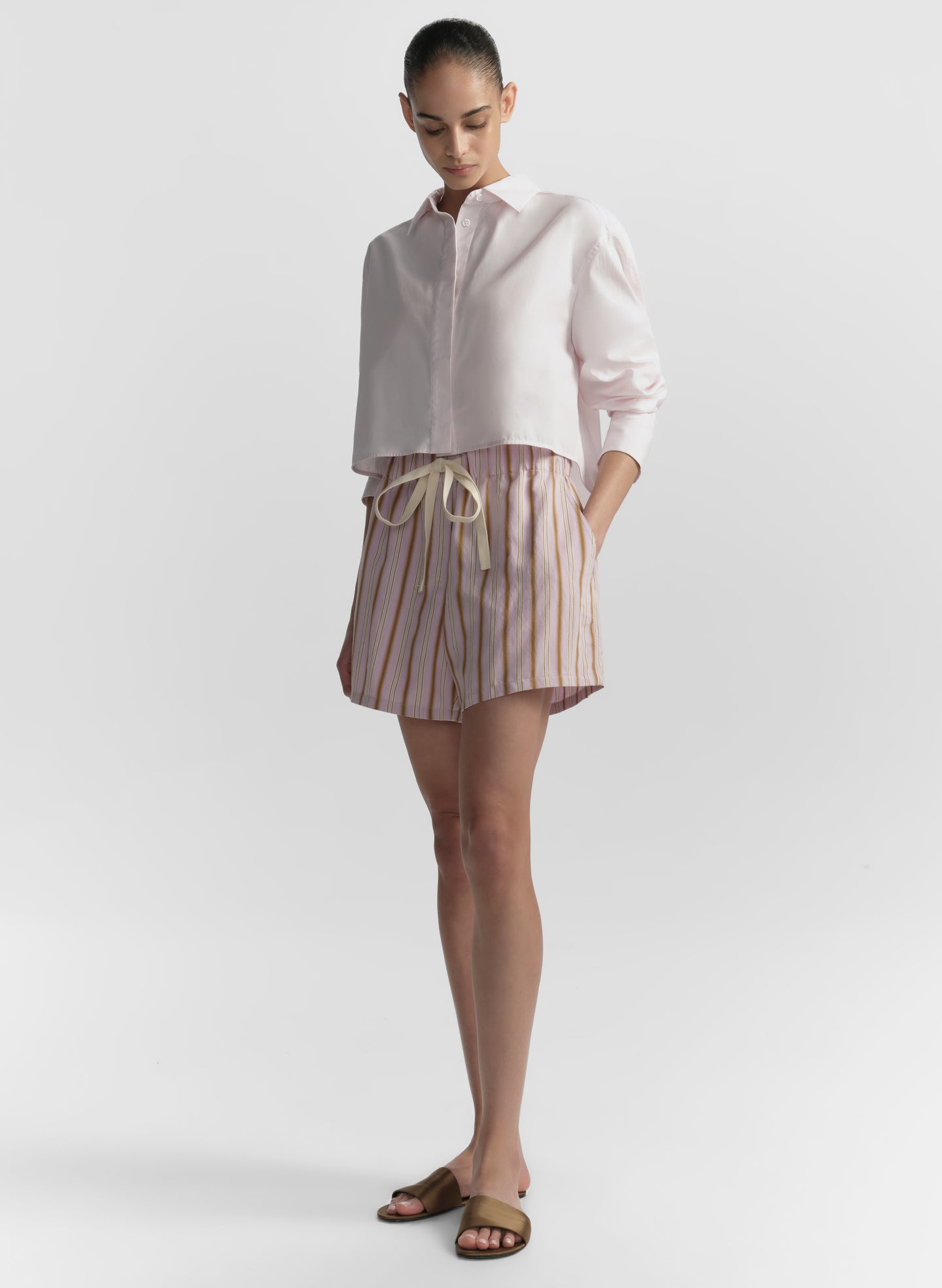 Woman wearing a light pink shirt and striped shorts on a plain background