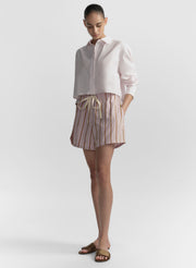 Woman wearing a light pink shirt and striped shorts on a plain background