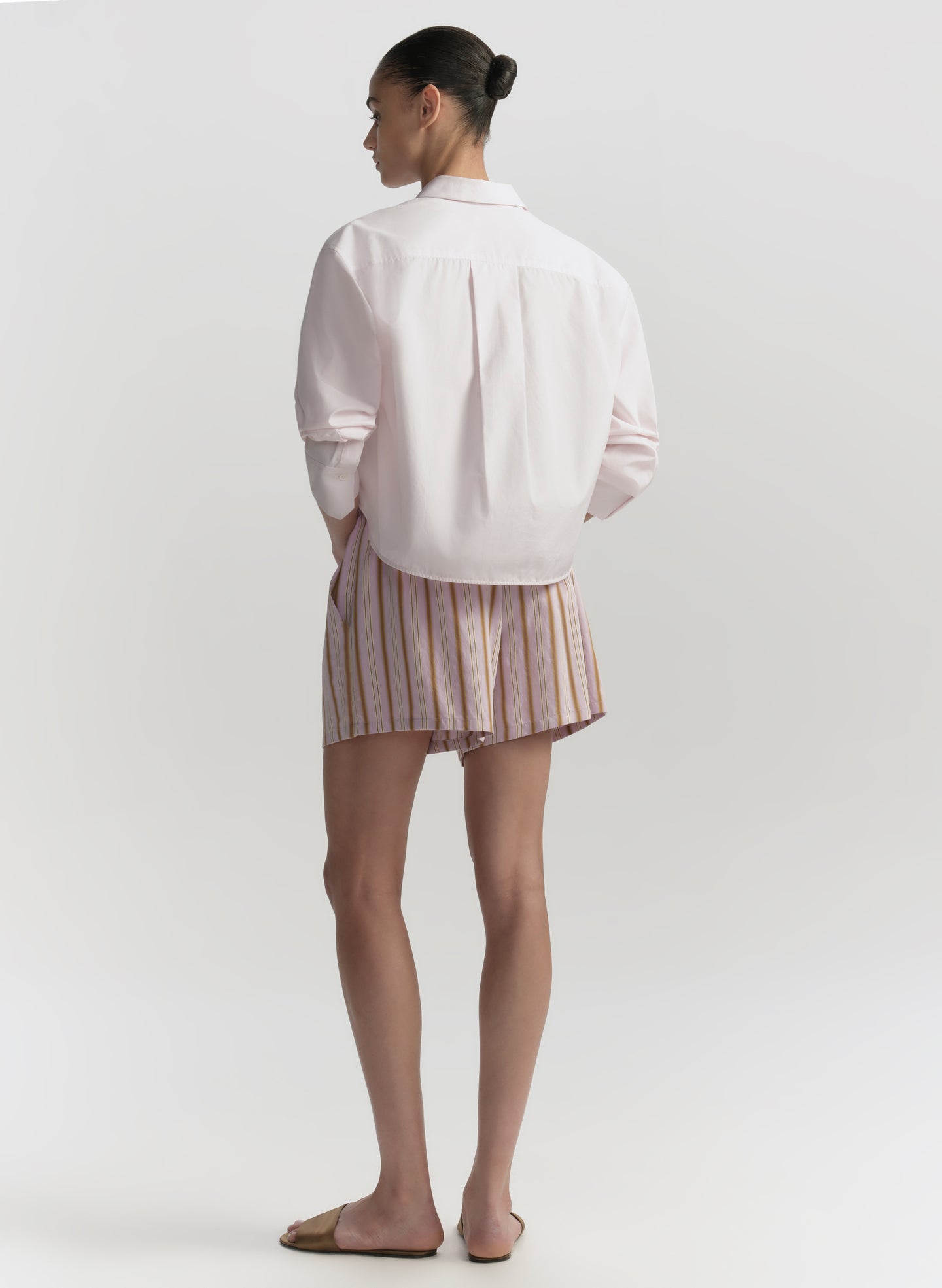 Person wearing a light pink shirt and striped shorts on a plain background