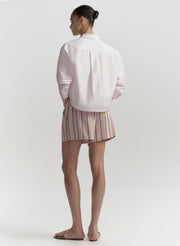 Person wearing a light pink shirt and striped shorts on a plain background