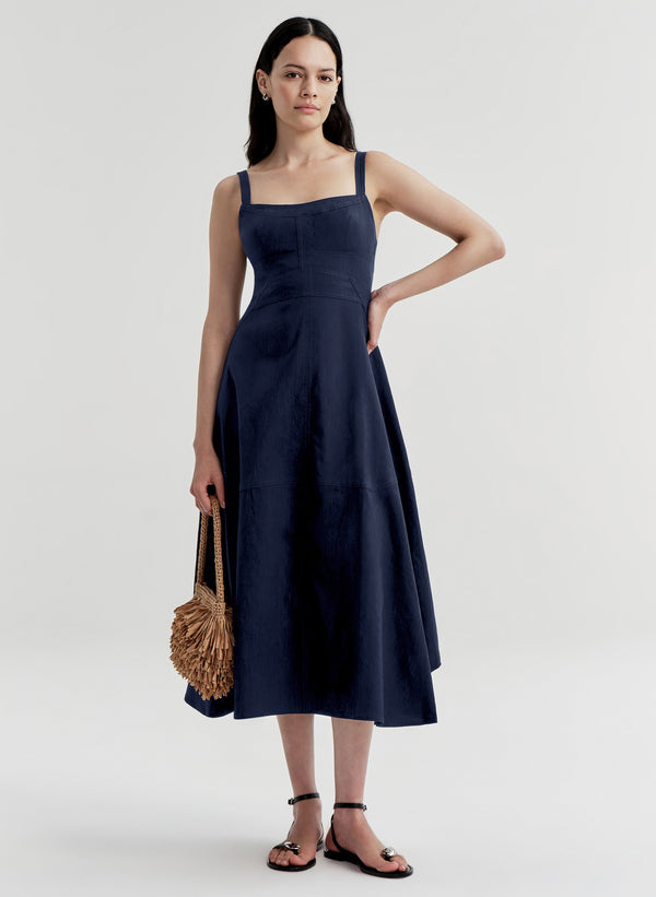 Woman wearing a navy blue dress holding a woven bag on a white background