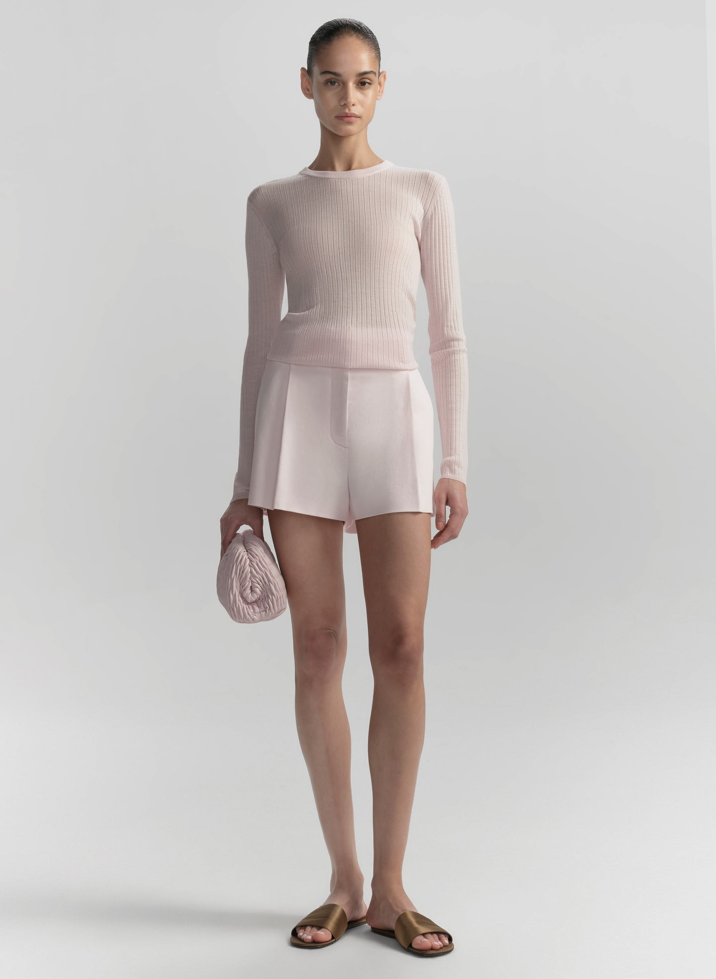 Woman wearing a light pink sweater and shorts set on a white background