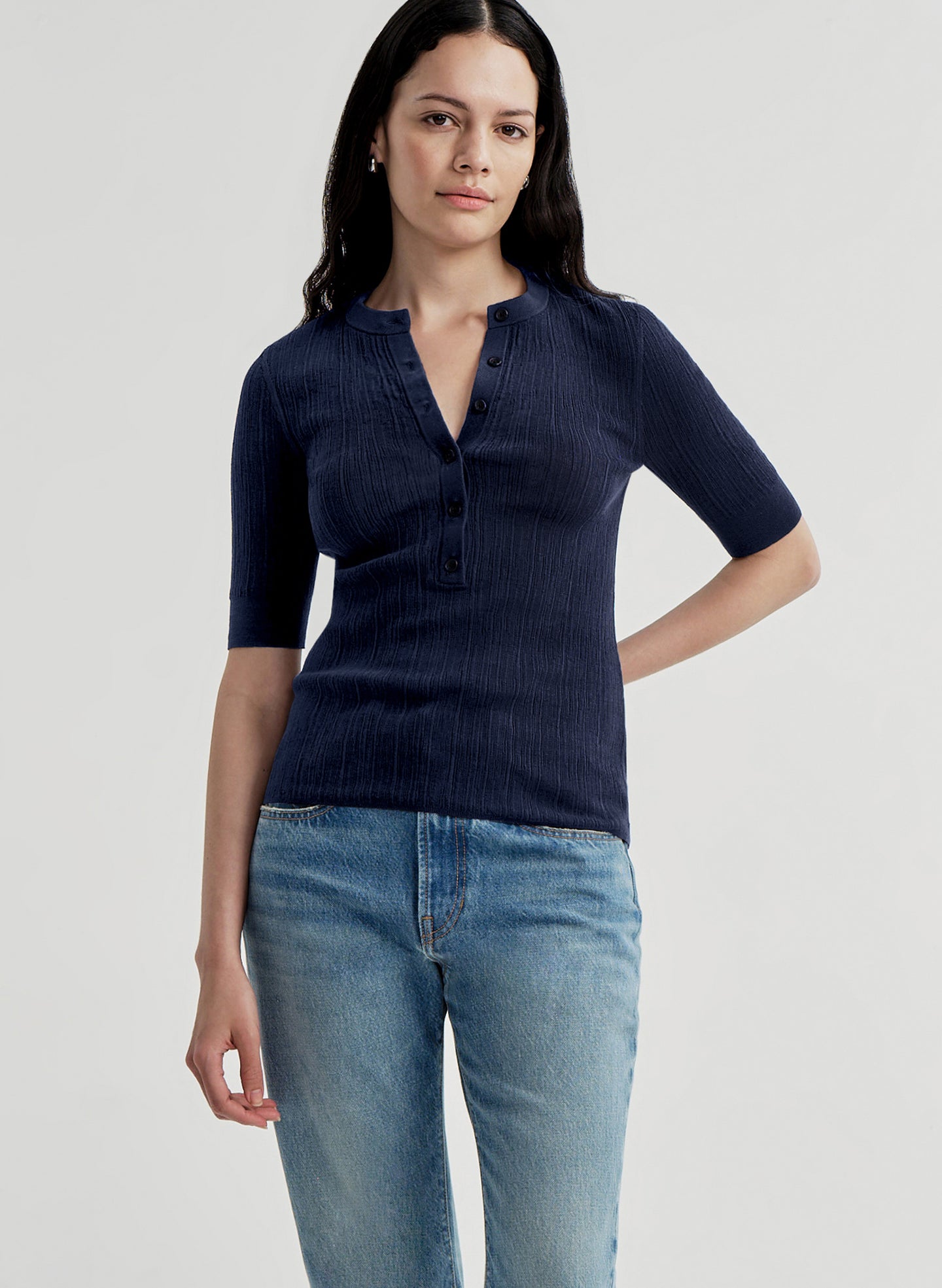 Woman wearing a navy blue shirt and light blue jeans on a plain background