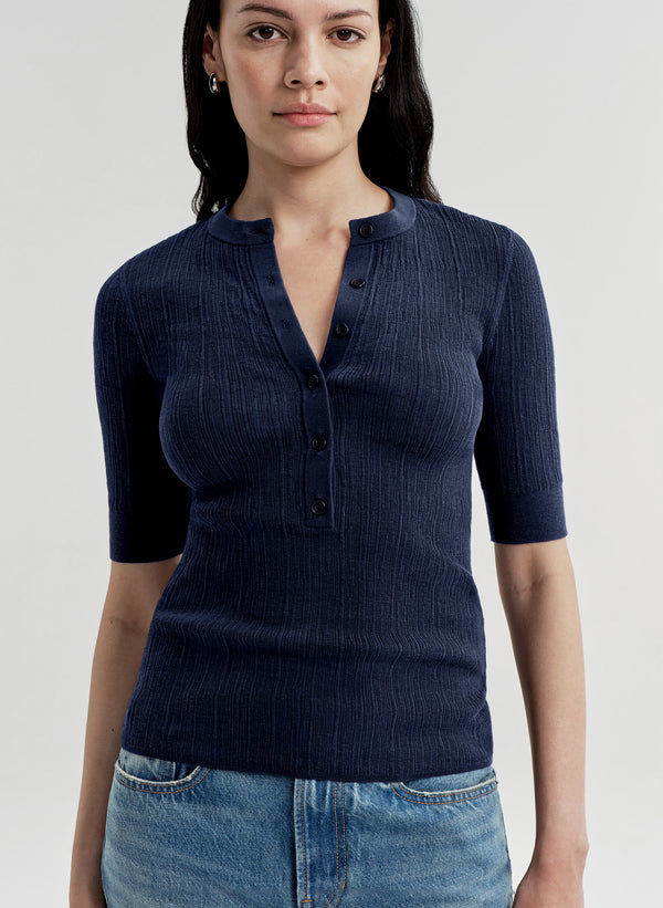 Woman wearing a navy blue ribbed knit shirt with short sleeves on a light gray background