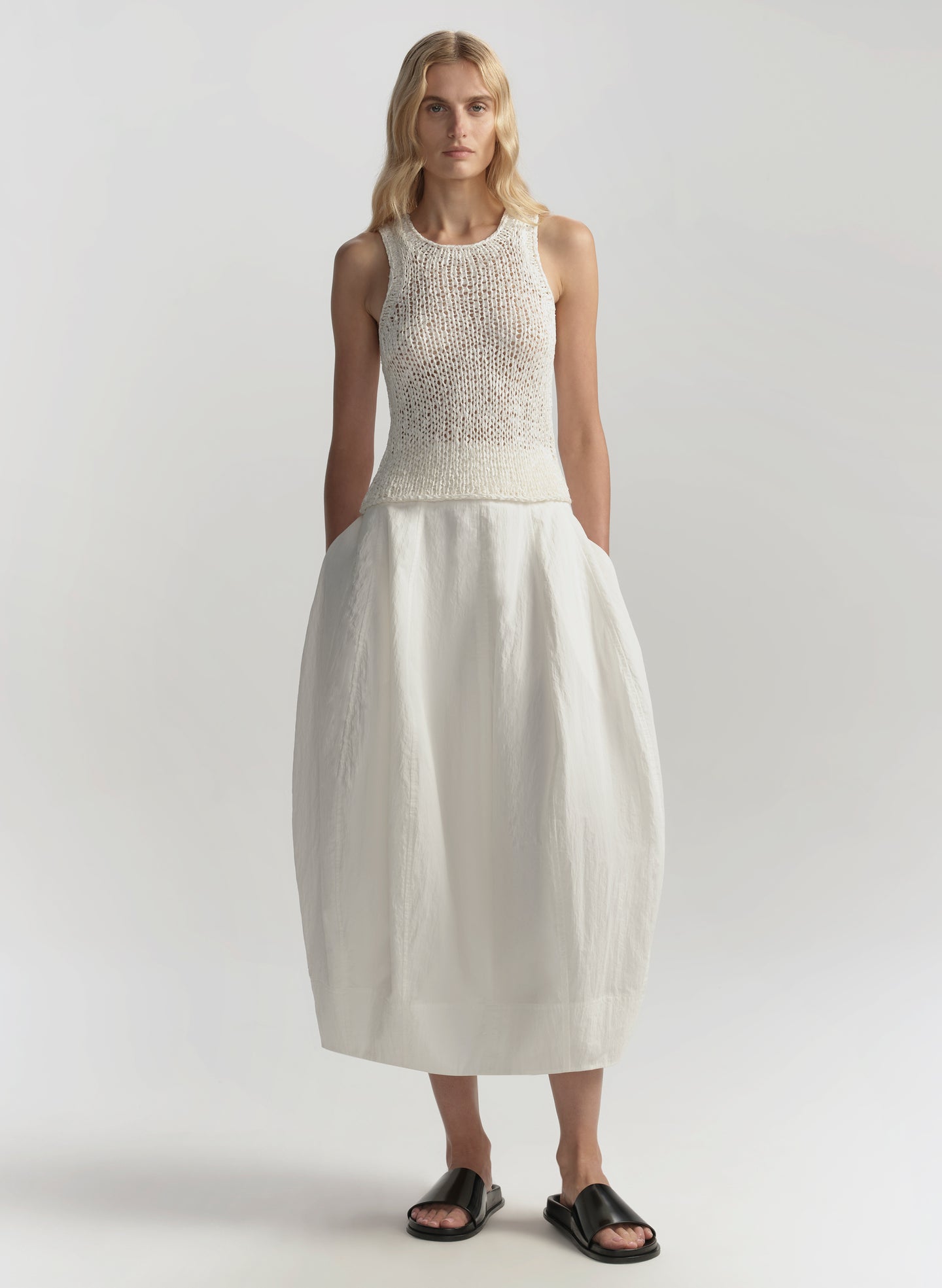 Woman wearing a white sleeveless top and skirt on a plain background