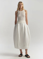 Woman wearing a white sleeveless top and skirt on a plain background