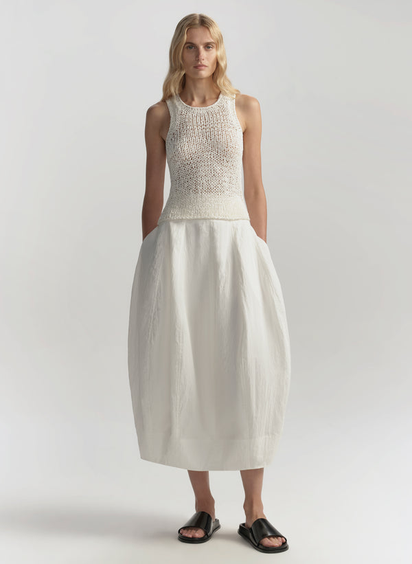 Woman wearing a white sleeveless top and skirt on a plain background