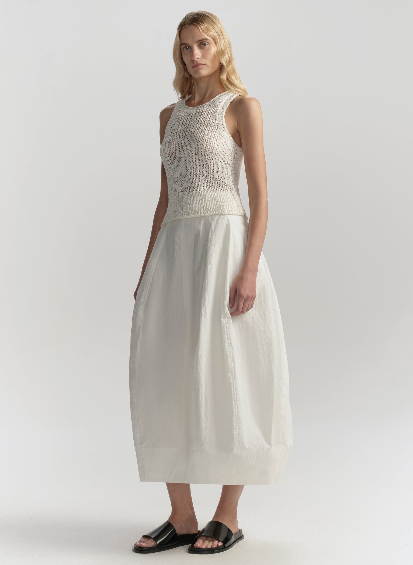 Woman wearing a white sleeveless top and skirt on a plain background