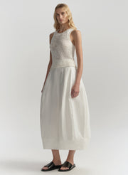 Woman wearing a white sleeveless top and skirt on a plain background
