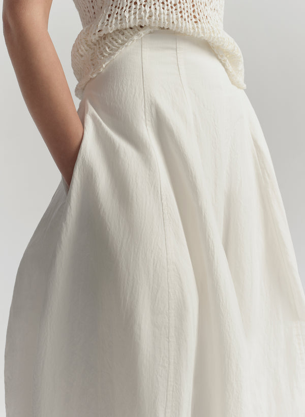 Person wearing a white skirt and light-colored top against a neutral background