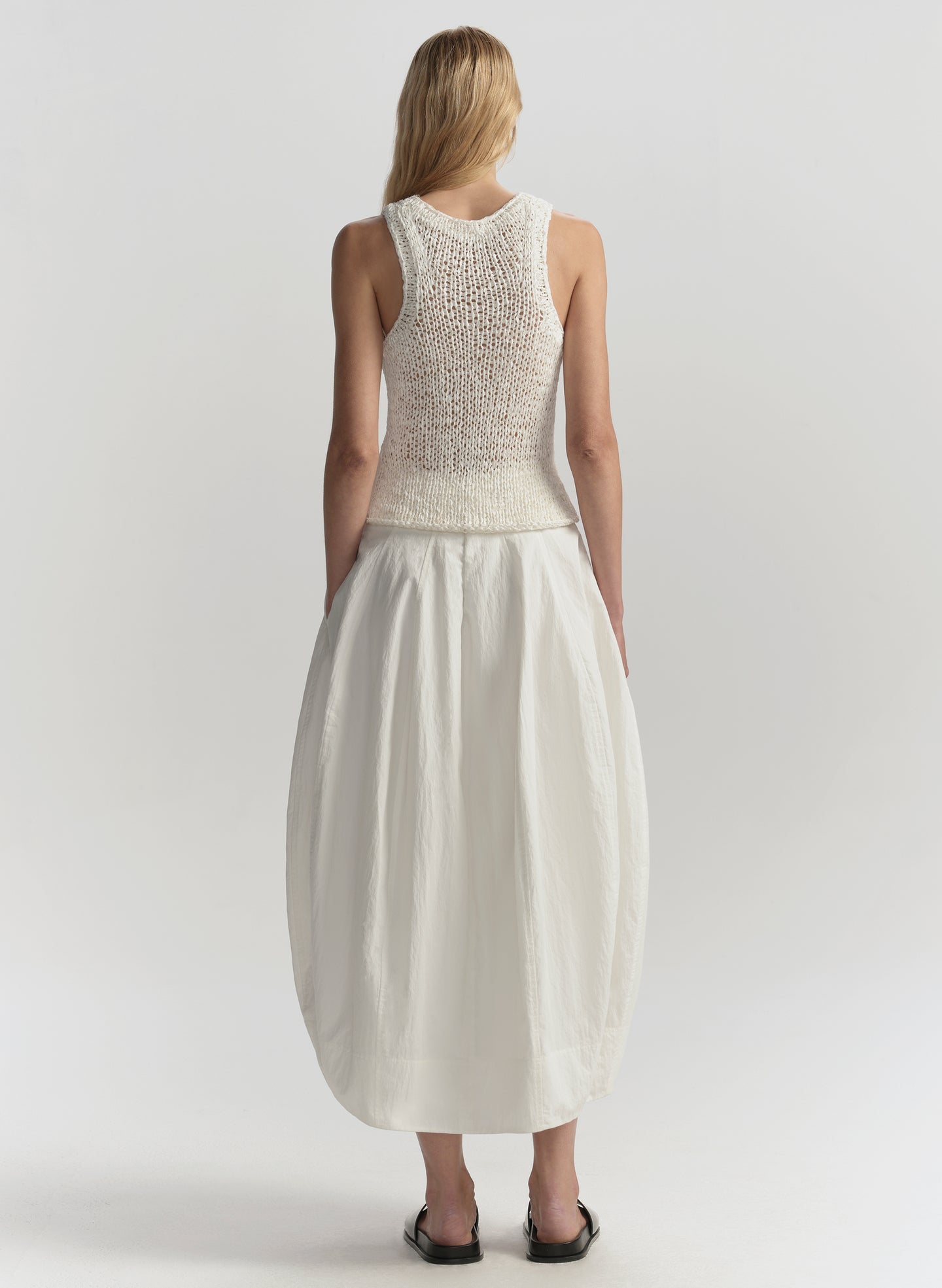 Woman wearing a white sleeveless top and skirt set on a plain background