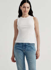Woman wearing a white sleeveless top and blue jeans on a light gray background