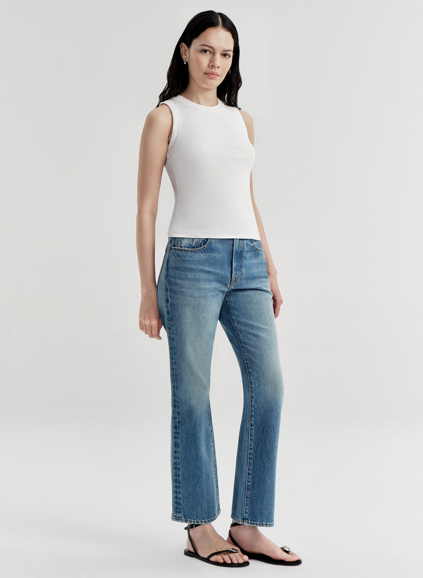 Woman wearing a white sleeveless top and blue jeans on a white background
