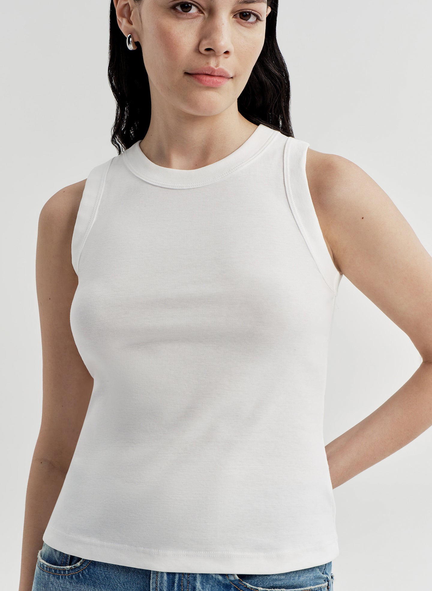 Woman wearing a white sleeveless top against a plain background