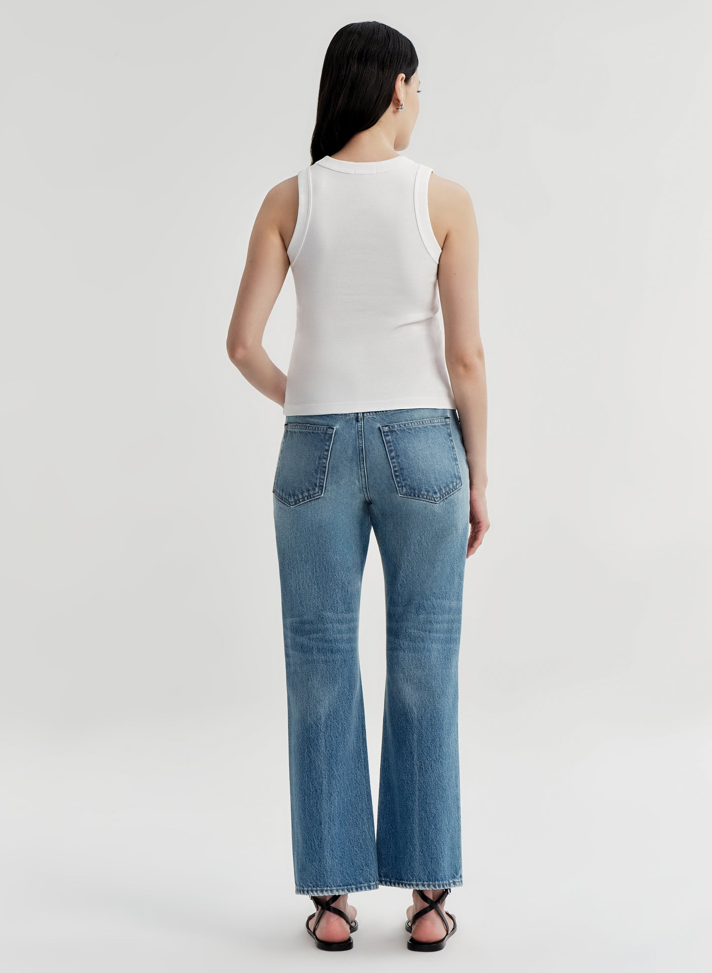 Person wearing a white sleeveless top and blue jeans on a light gray background