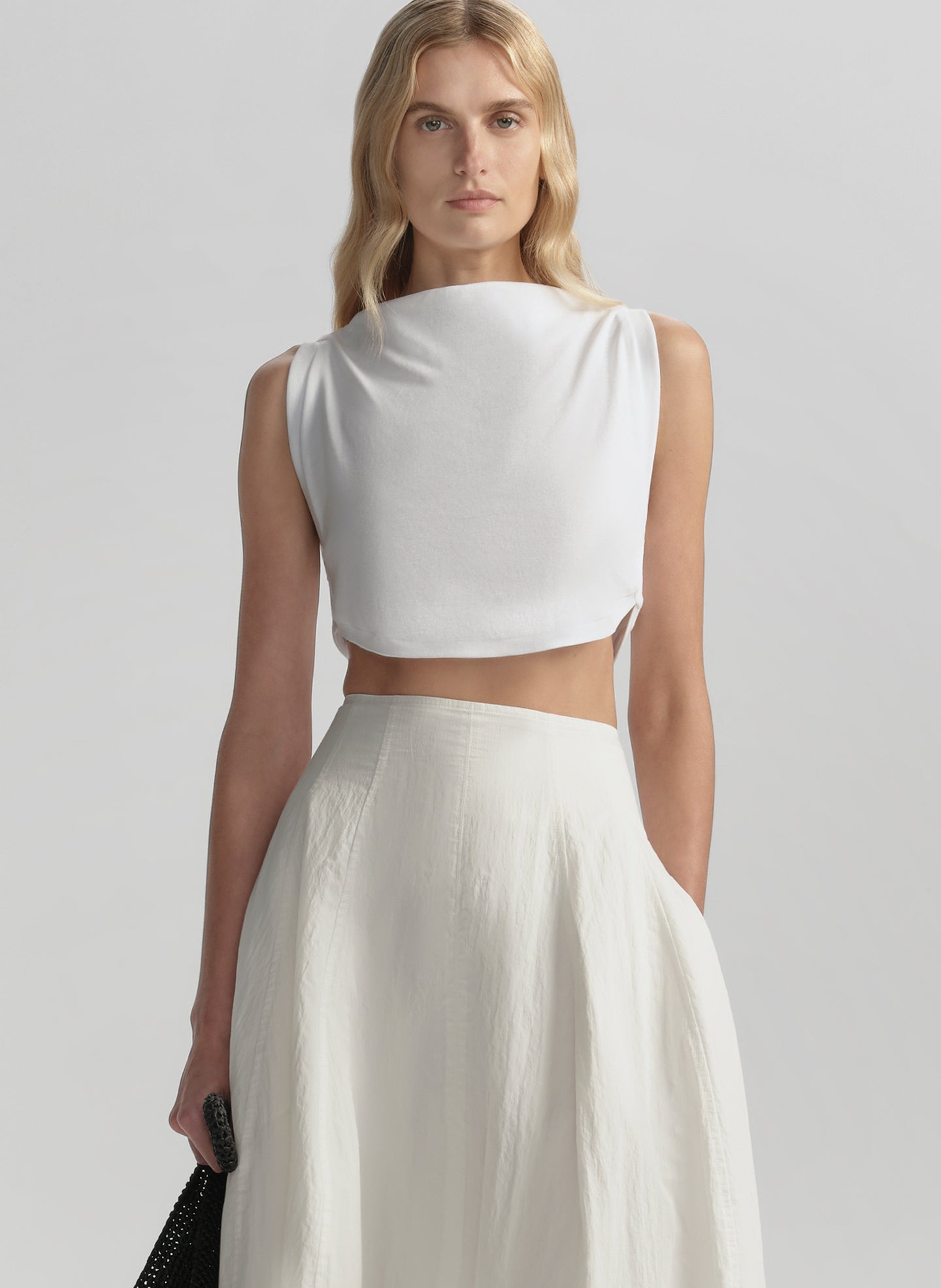 Woman wearing a white sleeveless top and skirt on a plain background