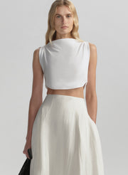 Woman wearing a white sleeveless top and skirt on a plain background