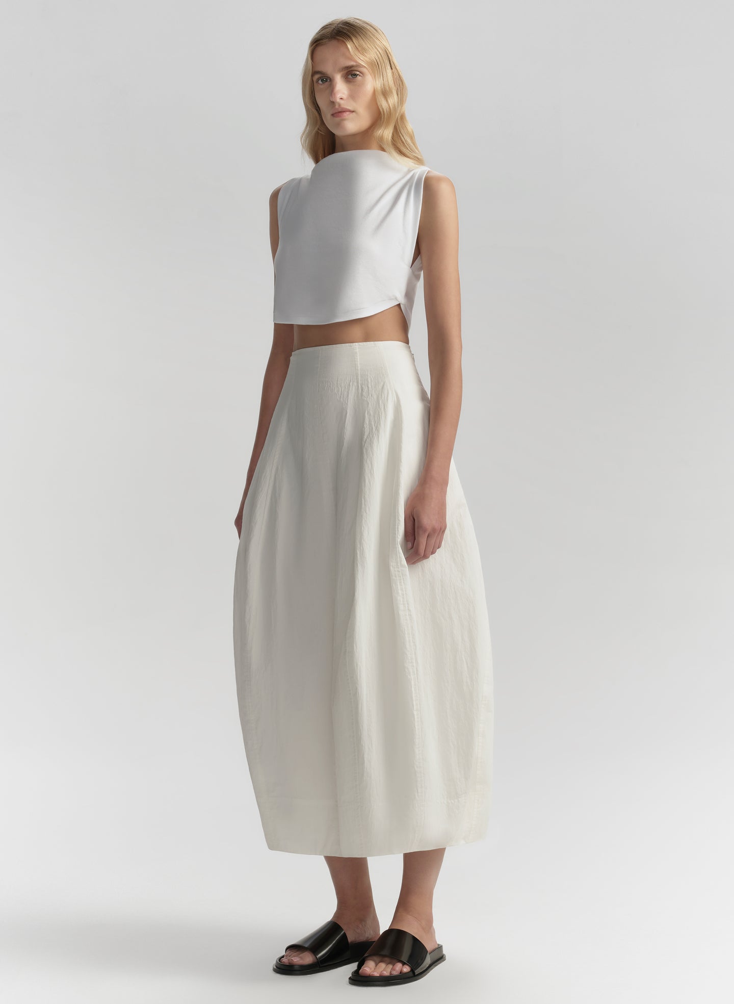 Woman wearing a white sleeveless top and cream skirt on a light gray background