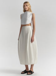 Woman wearing a white sleeveless top and cream skirt on a light gray background