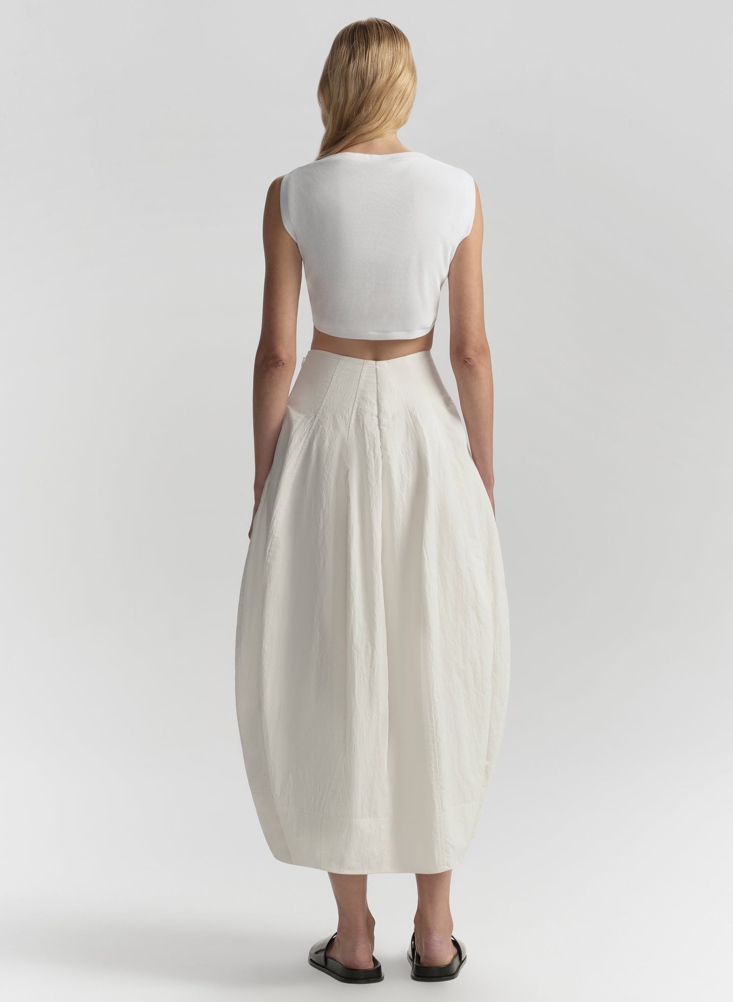 Person wearing a white sleeveless top and long cream skirt on a plain background
