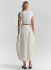 Person wearing a white sleeveless top and long cream skirt on a plain background