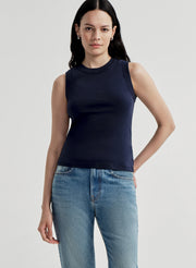 Woman wearing a blue sleeveless top and blue jeans on a light gray background