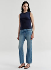 Woman wearing a navy sleeveless top and light blue jeans on a white background