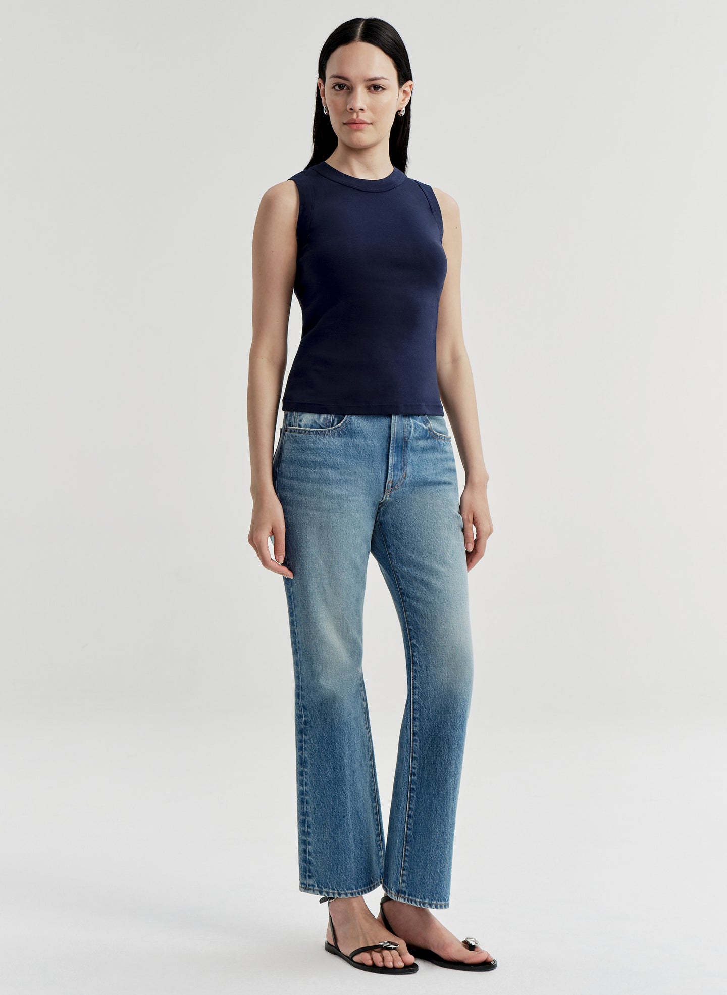 Woman wearing a navy sleeveless top and light blue jeans on a white background