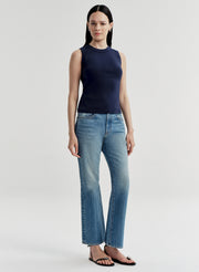 Woman wearing a navy sleeveless top and light blue jeans on a white background
