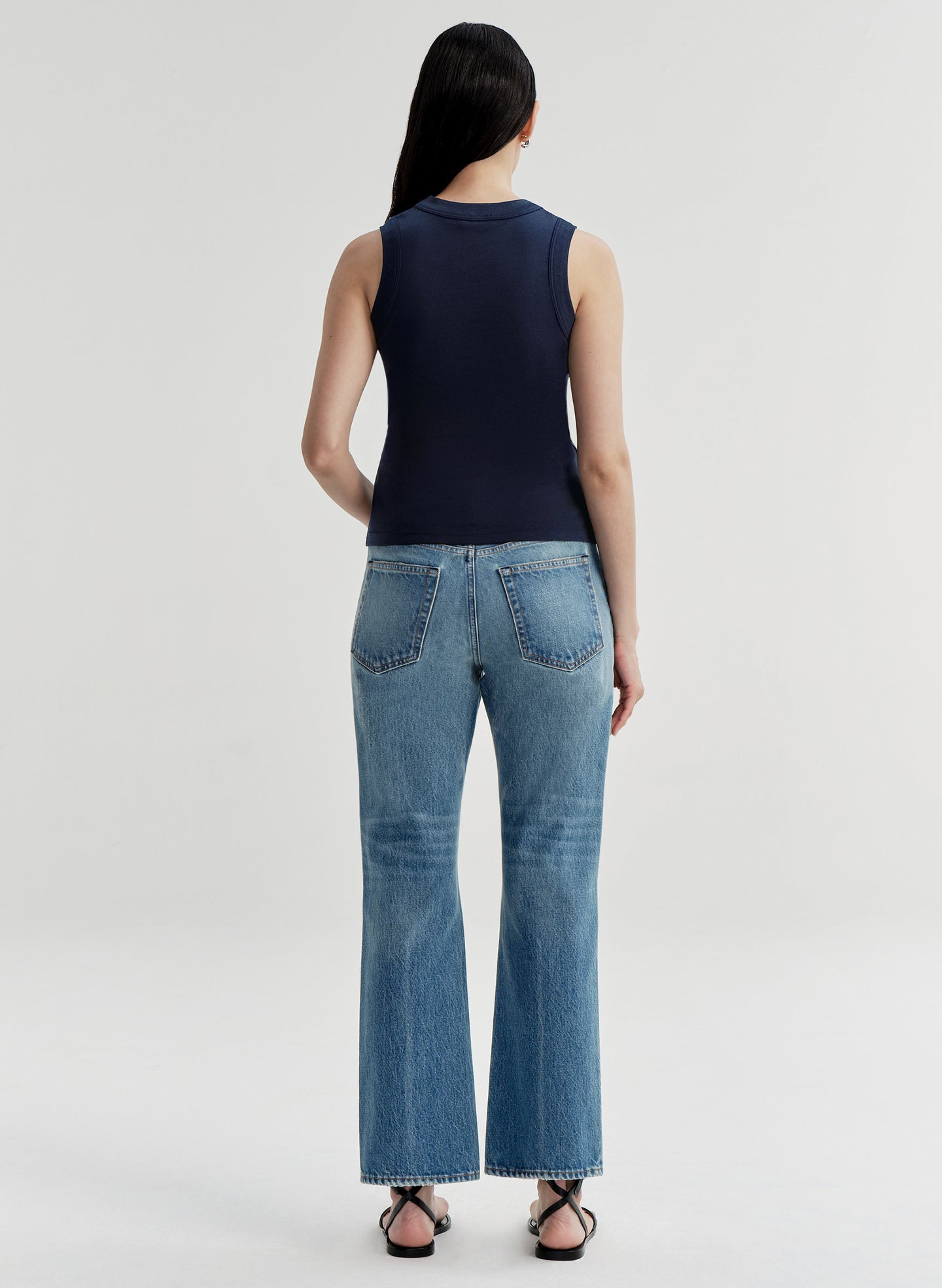 Woman wearing a navy sleeveless top and blue jeans on a white background