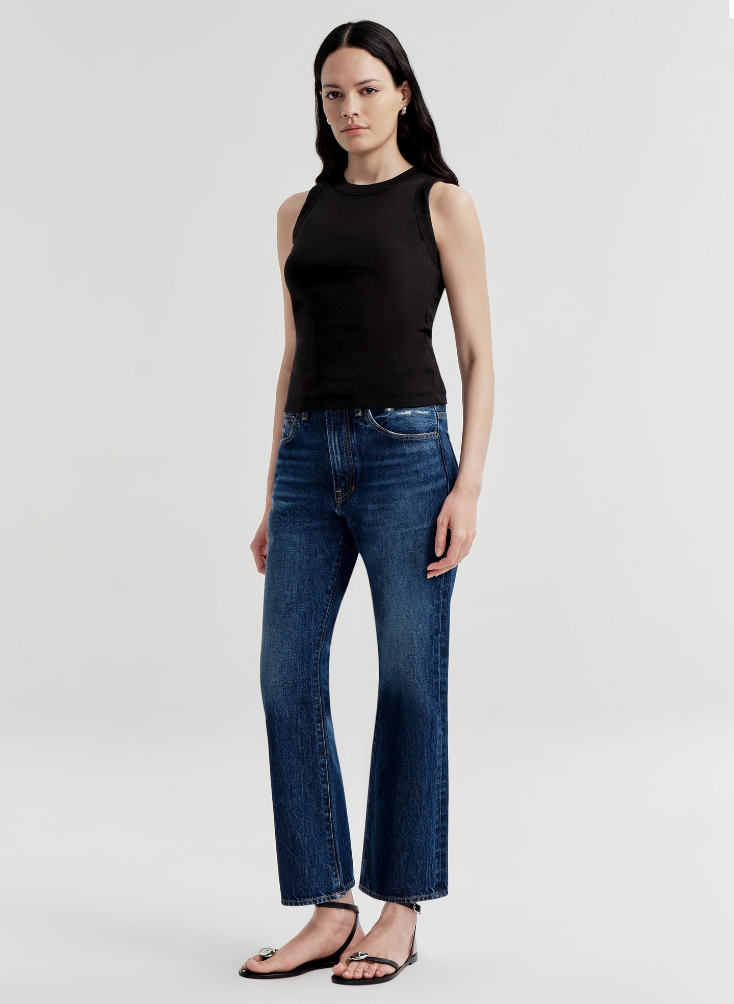 Woman wearing a black sleeveless top and blue jeans on a white background
