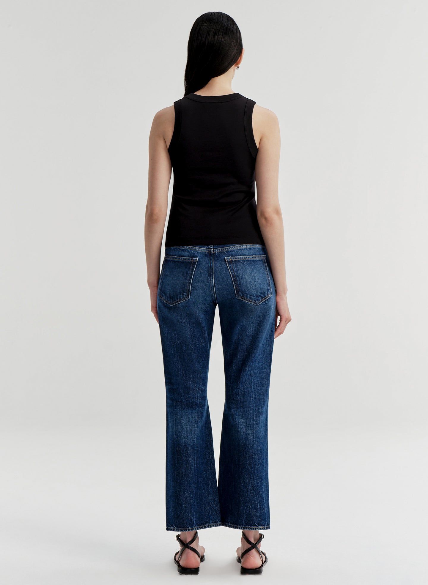 Woman wearing a black sleeveless top and blue jeans on a white background