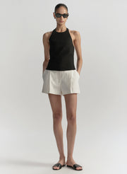 Woman wearing a black sleeveless top and white shorts on a plain background