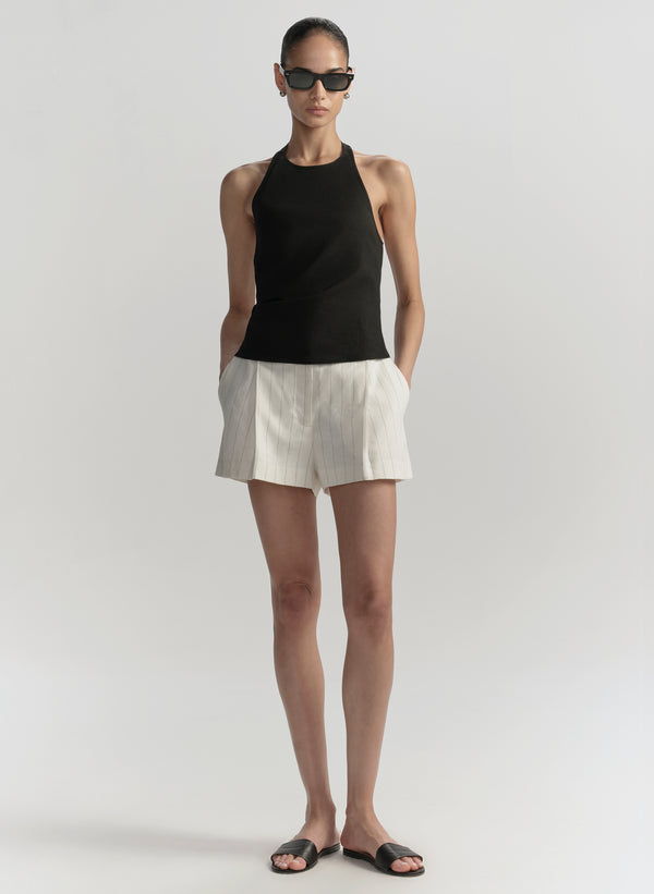 Woman wearing a black sleeveless top and white shorts on a plain background