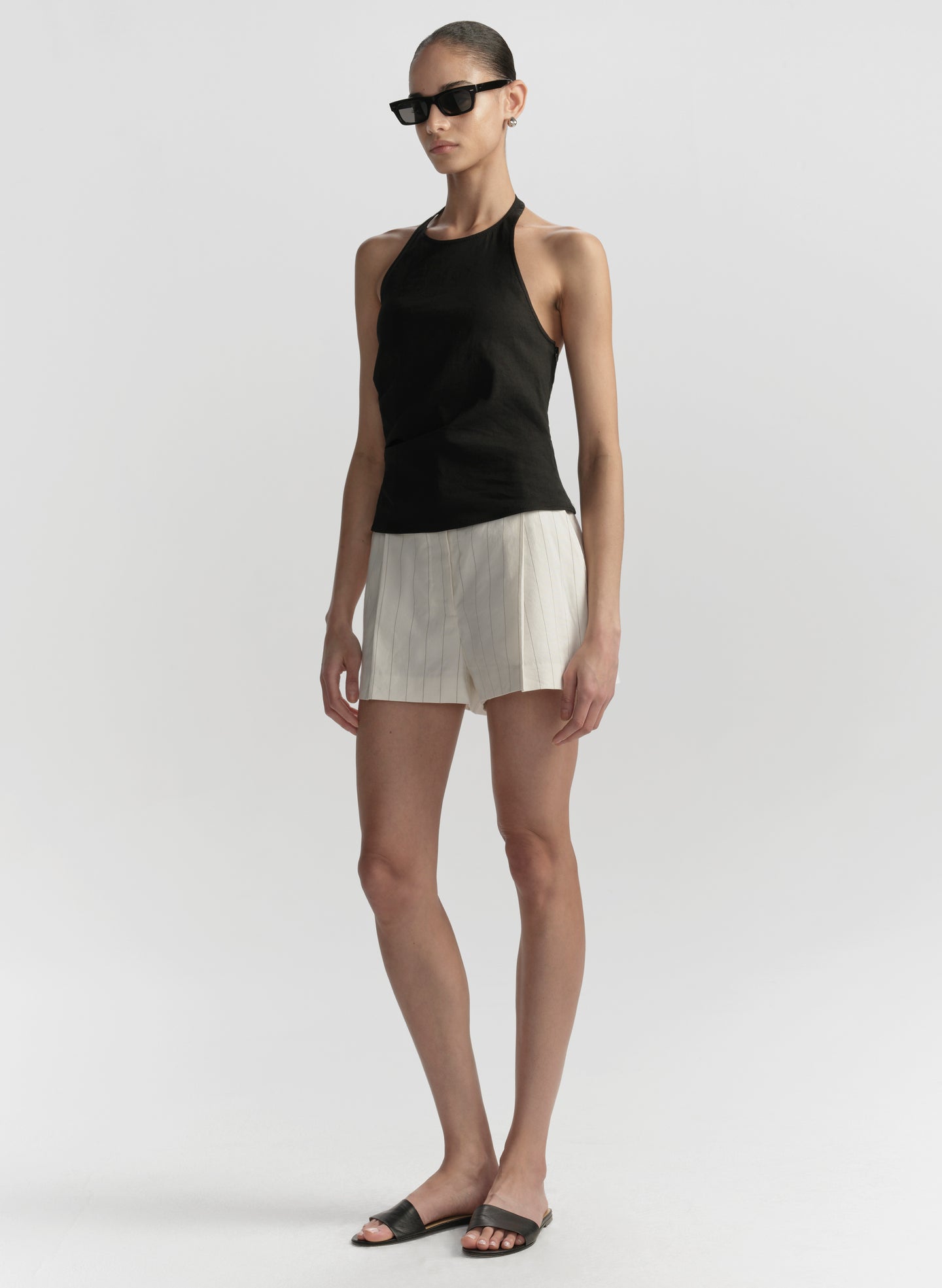 Woman wearing a black sleeveless top and white shorts on a plain background