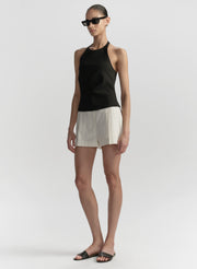 Woman wearing a black sleeveless top and white shorts on a plain background