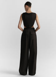 Woman wearing a black sleeveless top and wide-leg pants on a white background