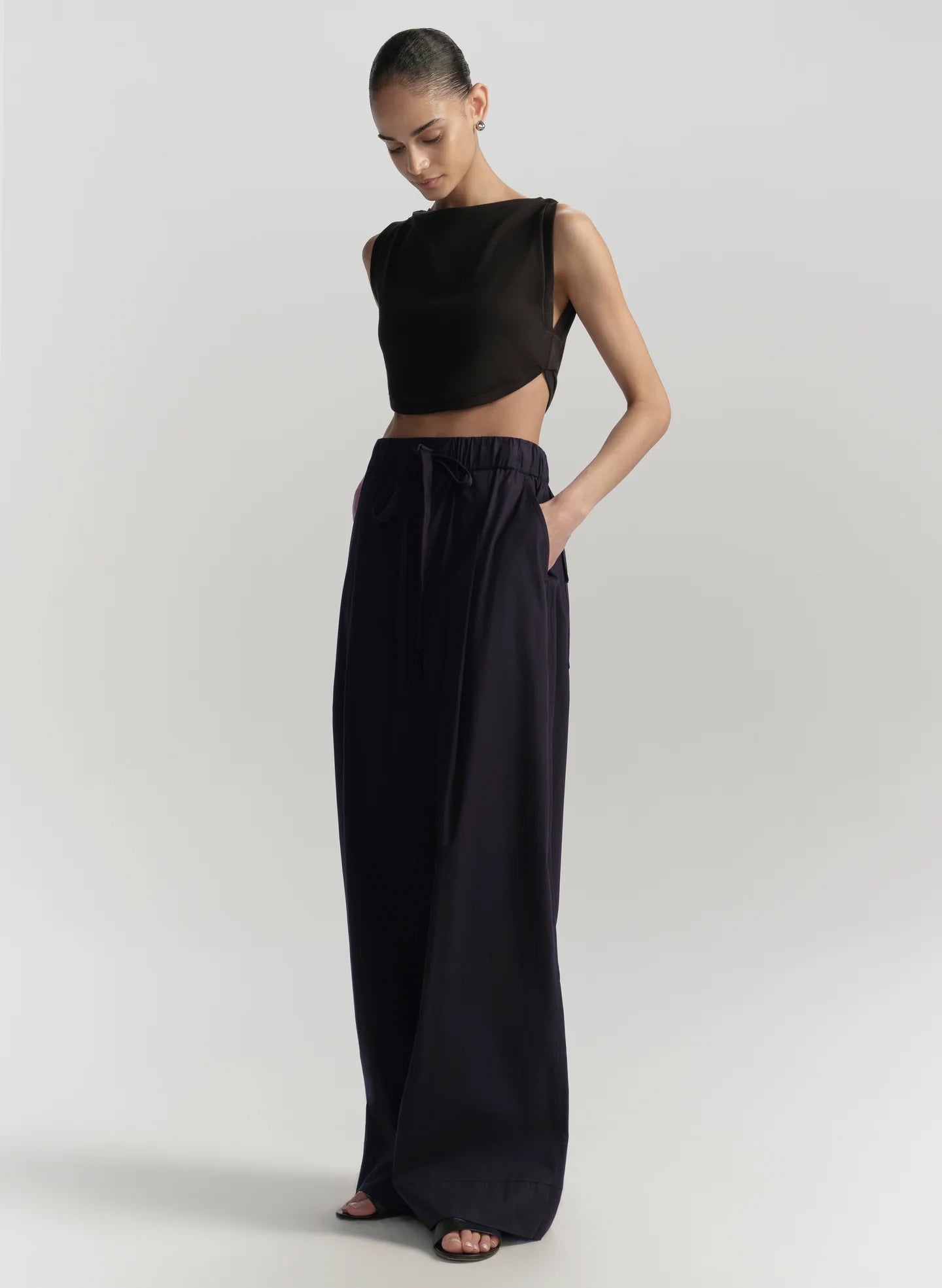 Woman wearing a black sleeveless top and long blue pants on a light gray background