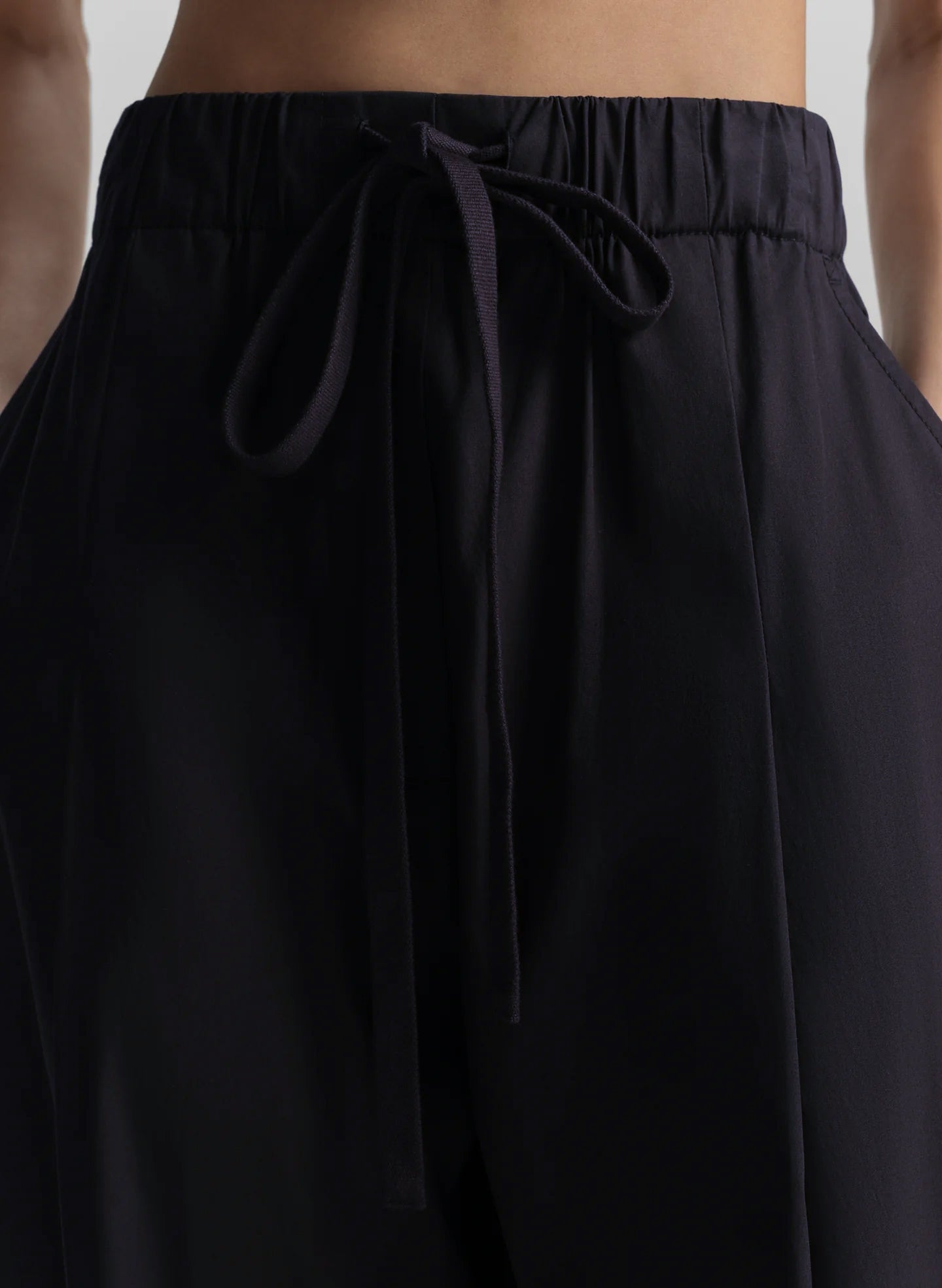 Woman wearing a black sleeveless top and long blue pants on a light gray background