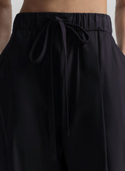 Woman wearing a black sleeveless top and long blue pants on a light gray background