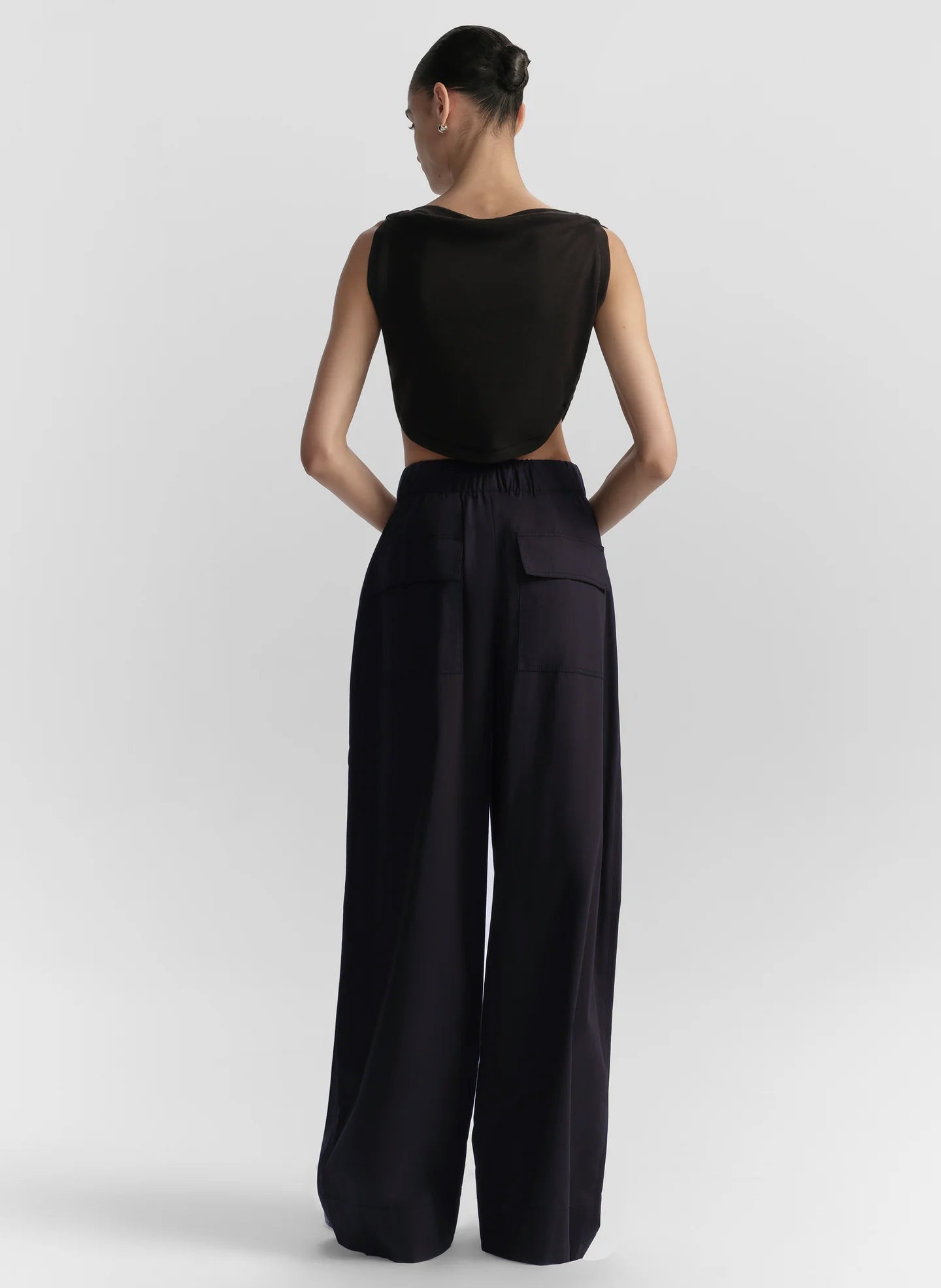 Woman wearing a black sleeveless top and long blue pants on a light gray background