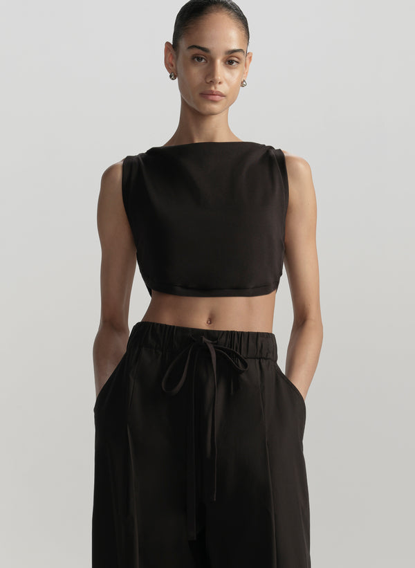 Woman wearing a black sleeveless top and black pants on a light gray background