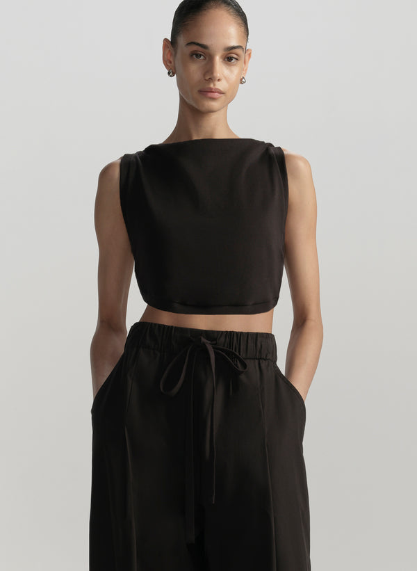 Woman wearing a black sleeveless top and black pants on a light gray background