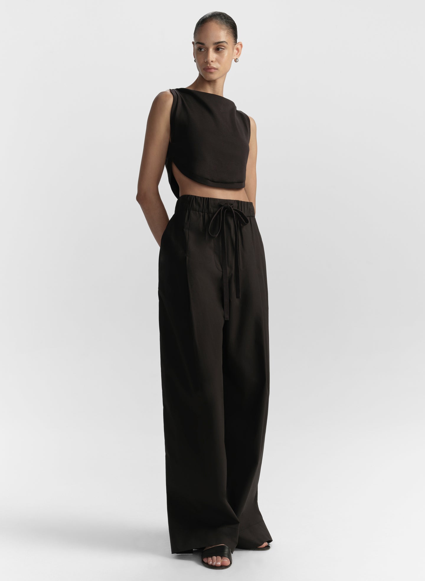 Woman wearing a black sleeveless top and wide-leg pants on a white background