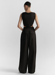 Woman wearing a black sleeveless top and wide-leg pants on a white background